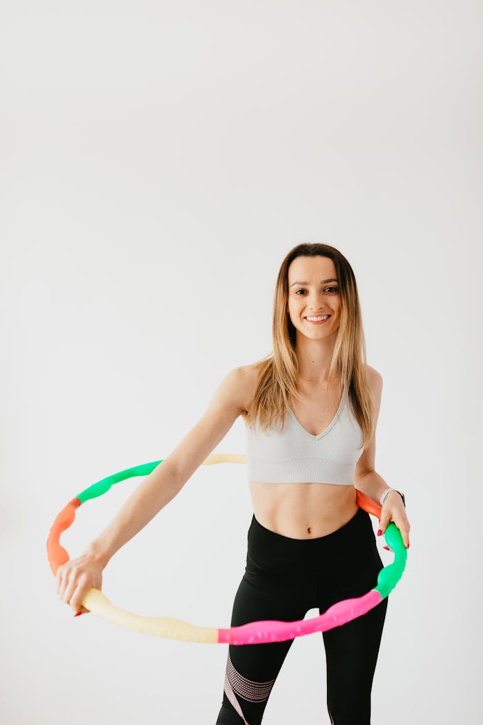 Smiling woman exercises with hula hoop in studio, showcasing fitness and vitality.